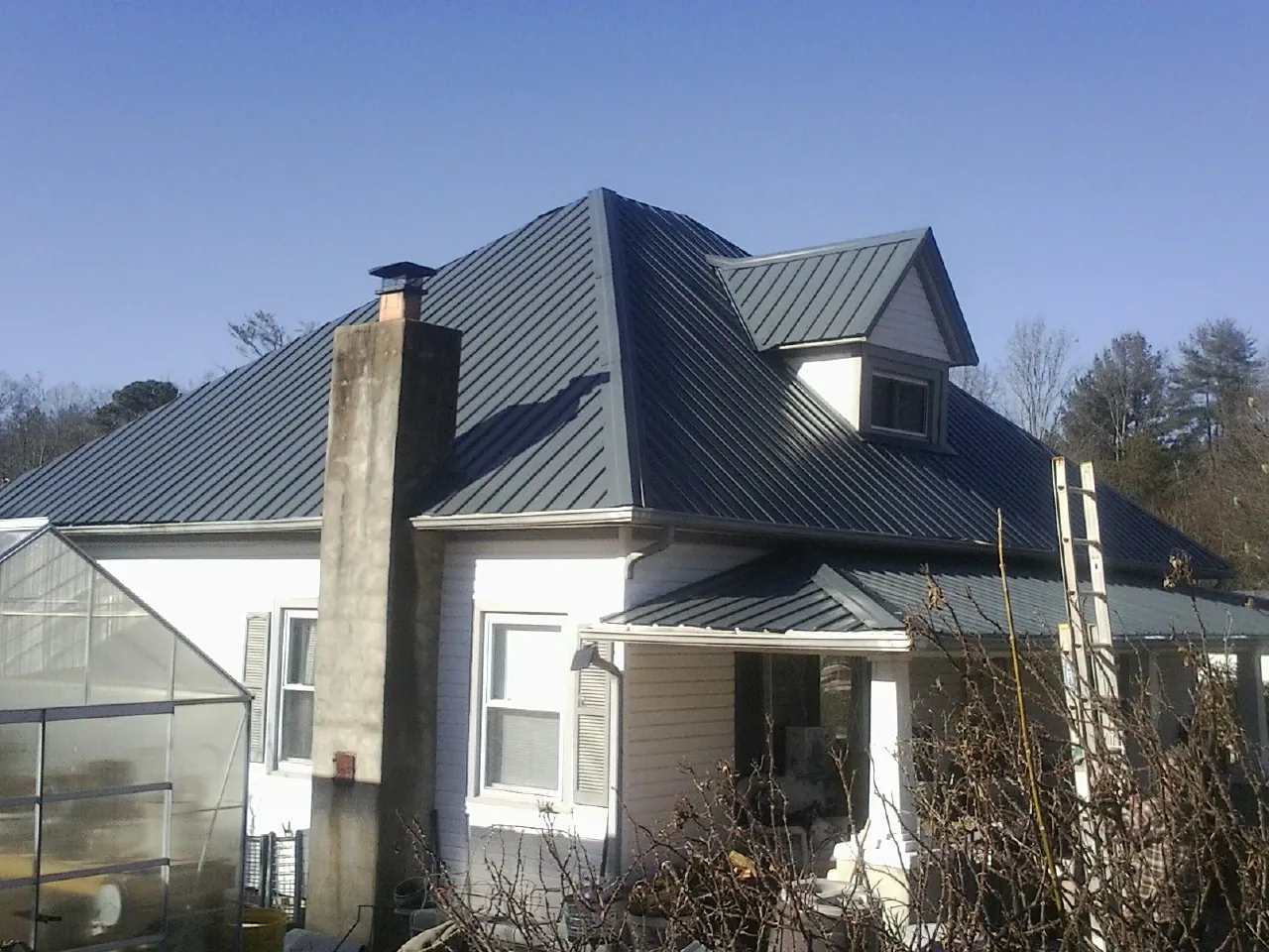 Dark blue standing seam metal roof on a white farmhouse with dormer — Slate & Tile Roof Repair by Roofing Brothers in Radiant