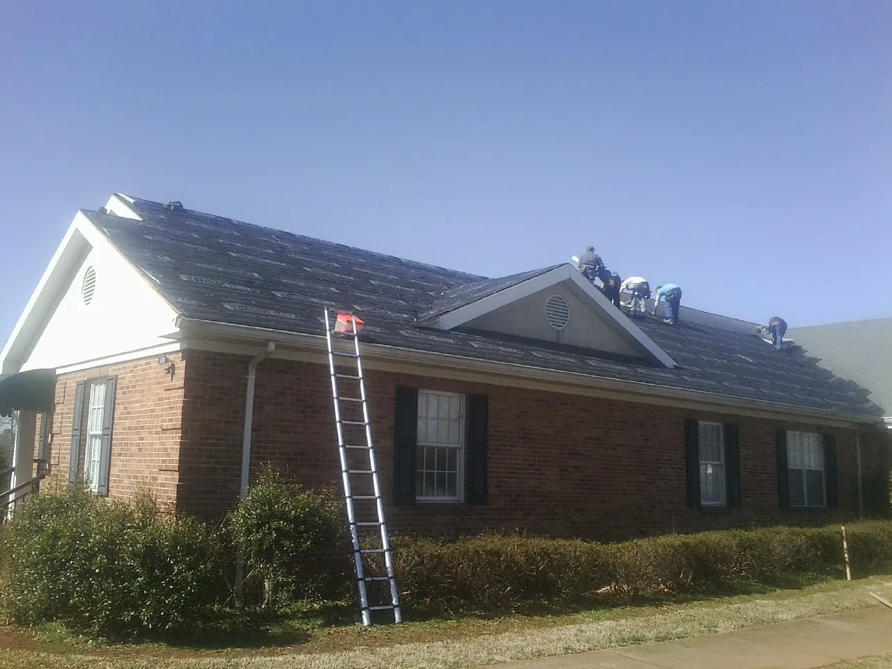 Crew tearing shingles off a brick ranch roof with a ladder set — Emergency Roof Repair work by our crew in Radiant