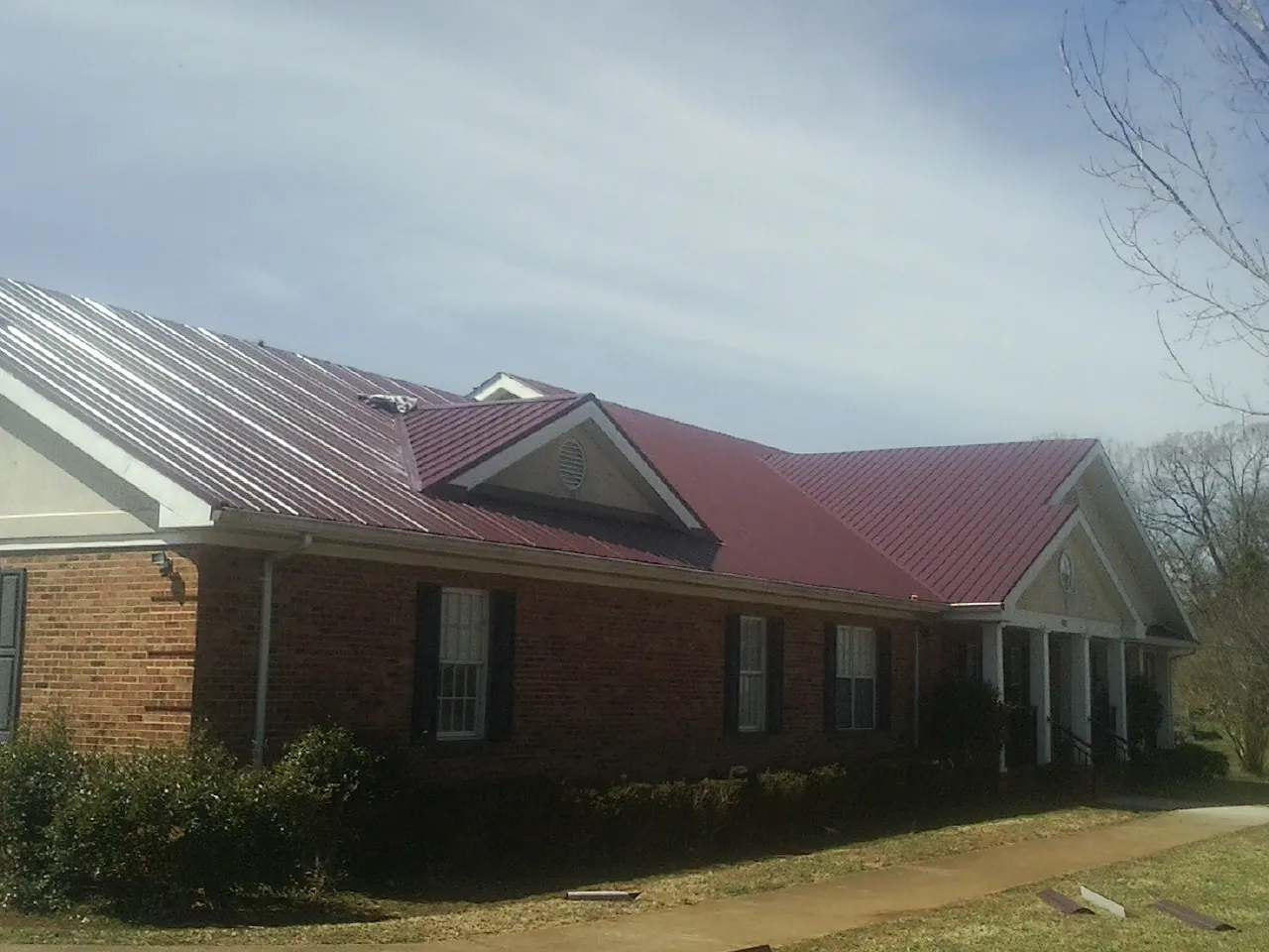 Red metal roof with gabled entries on a long brick building, from a Hail Damage Roof Repair job in Radiant
