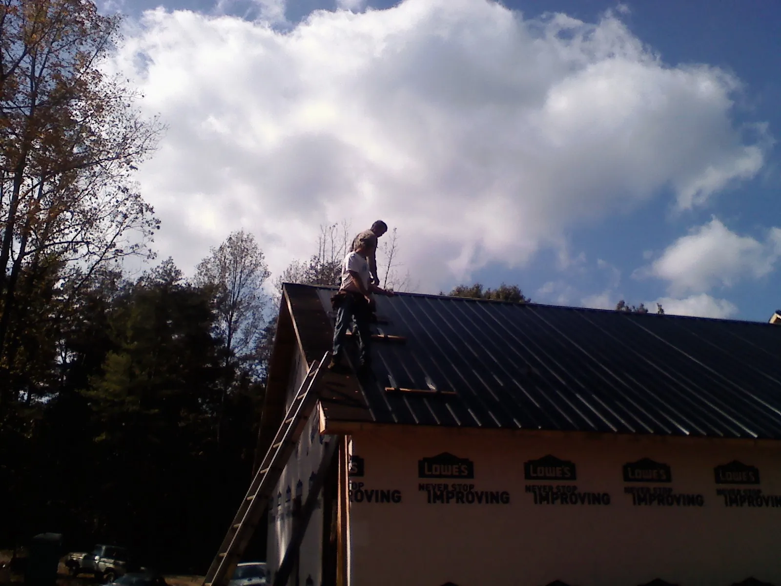 Roofer fastening dark metal panels high against a cloudy sky, from a Roof Inspection job in Radiant
