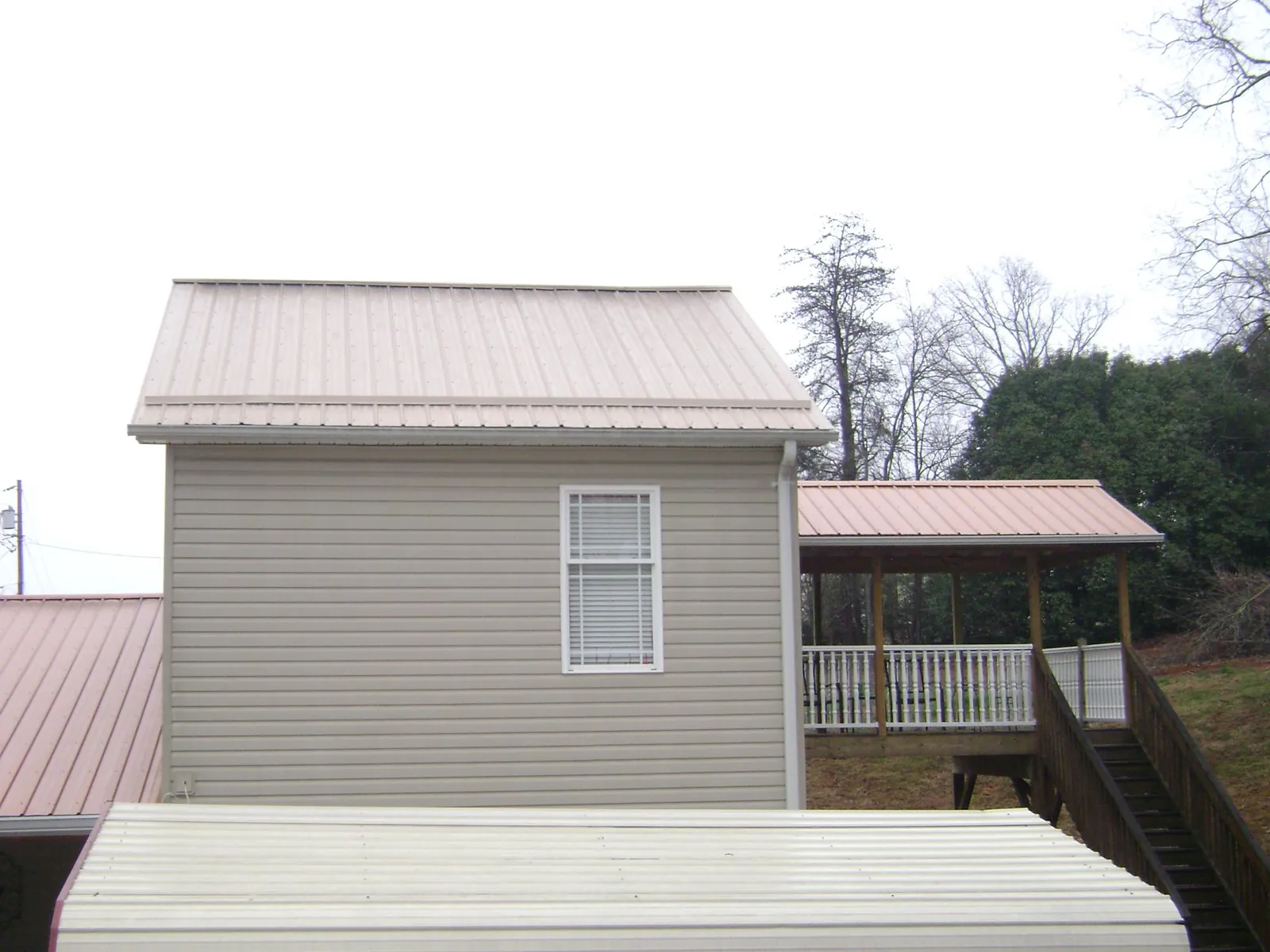 Tan metal roofs on a two story addition and attached porch, from a Roof Replacement job in Radiant